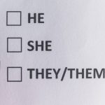 Three checkboxes printed on a piece of paper, one beside “he,” one beside “she” and one beside “they/them.” The tip of a felt-tip pen hovers over the paper.