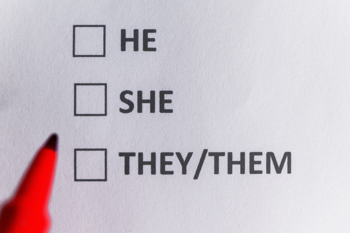 Three checkboxes printed on a piece of paper, one beside “he,” one beside “she” and one beside “they/them.” The tip of a felt-tip pen hovers over the paper.