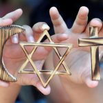 Hands hold large gold symbols associated with religious observances. From left to right, the hands hold the Muslim crescent, the Jewish star, and the Christian cross.