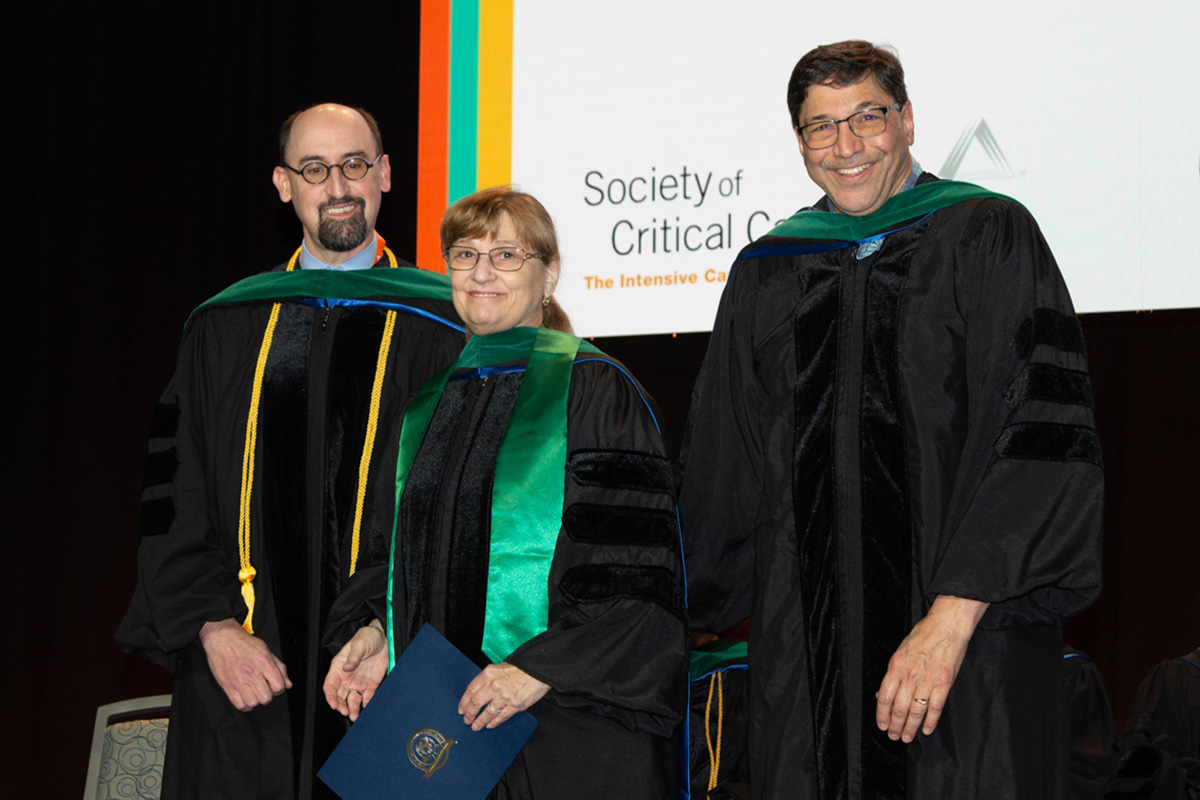 Dr. Sandralee Blosser, standing between two other people, holds an award after being conferred the title of Master of Critical Care Medicine on Jan. 21, 2024, at a convocation in Phoenix, Arizona.