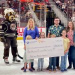 People are gathered around a big check for a photo at an ice hockey game