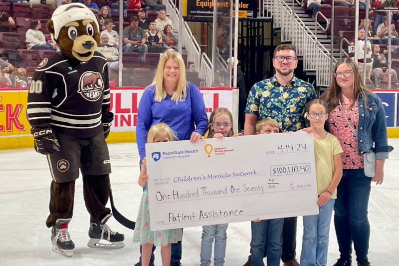 People are gathered around a big check for a photo at an ice hockey game