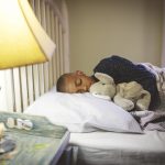 Boy holding a stuffed animal sleeping on a bed with a light on