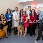 A group of people, and two dogs, smile for a photo before cutting the ribbon to open a new hospital unit