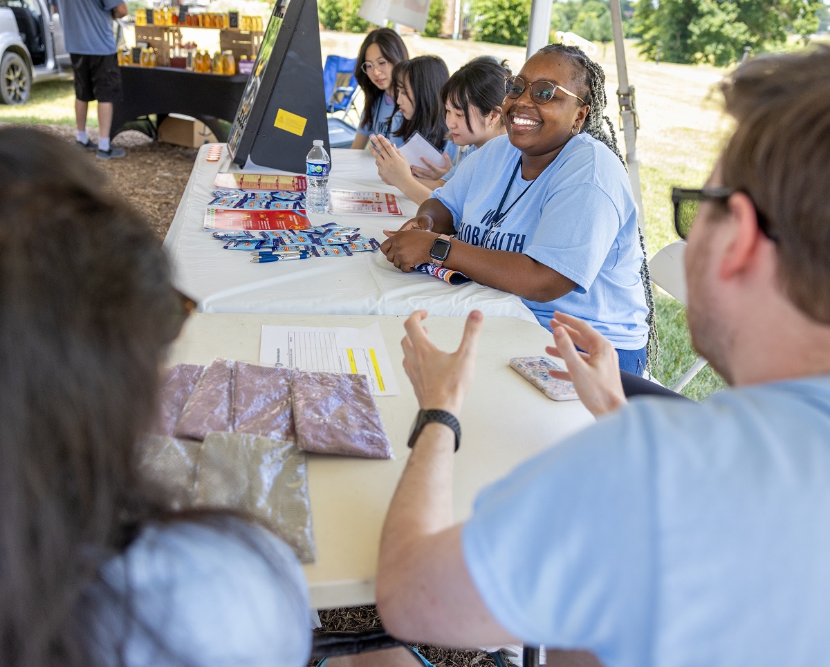 A group of students wearing matching shirts sit around a stand at a farmer's market