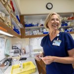 A pharmacist at Penn State Health's Holy Spirit Medical Center, stands smiling in the pharmacy, surrounded by shelves of medical supplies and charts.