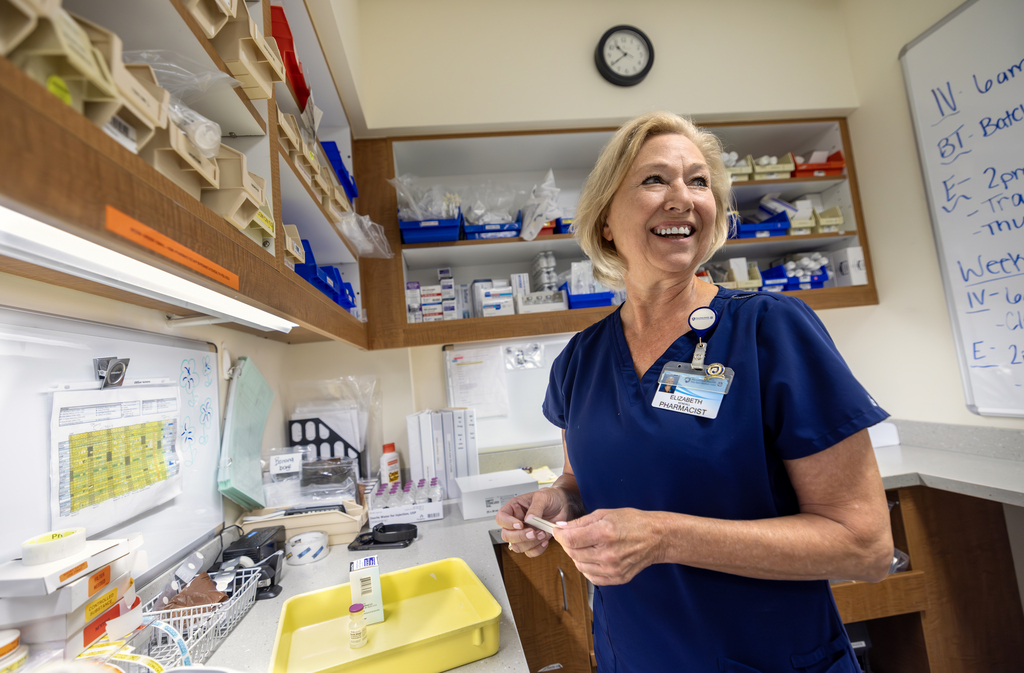 A pharmacist at Penn State Health's Holy Spirit Medical Center, stands smiling in the pharmacy, surrounded by shelves of medical supplies and charts.