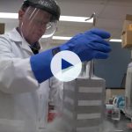 Neil Christensen works in the lab wearing a lab coat, gloves covering his hands and forearms, and a face shield.