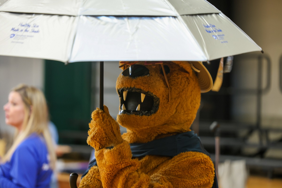 Someone dressed as the Penn State Nittany Lion raises an umbrella.