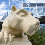 A close-up of a Nittany Lion statue with Hampden Medical Center in the background, slightly out of focus.