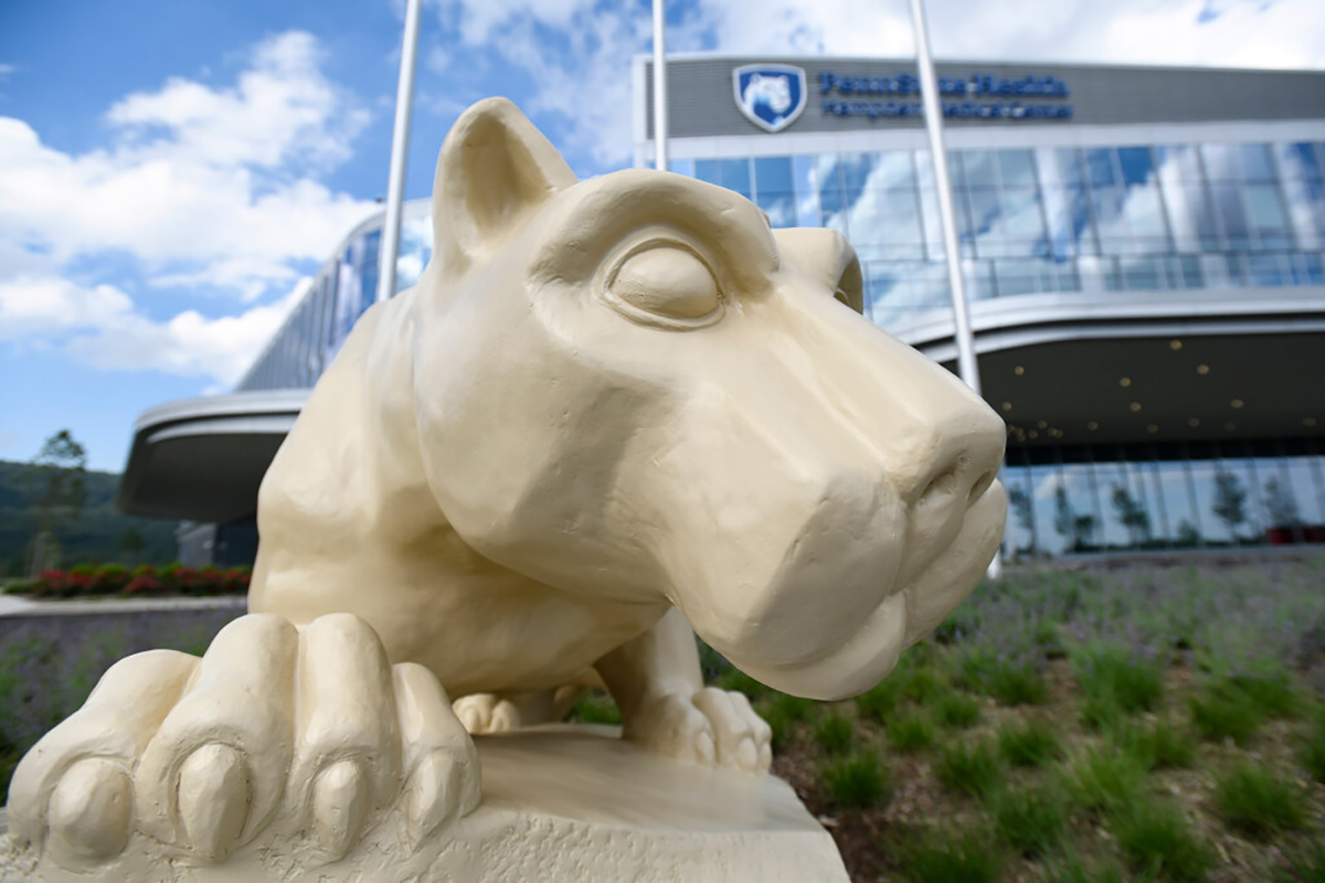 A close-up of a Nittany Lion statue with Hampden Medical Center in the background, slightly out of focus.