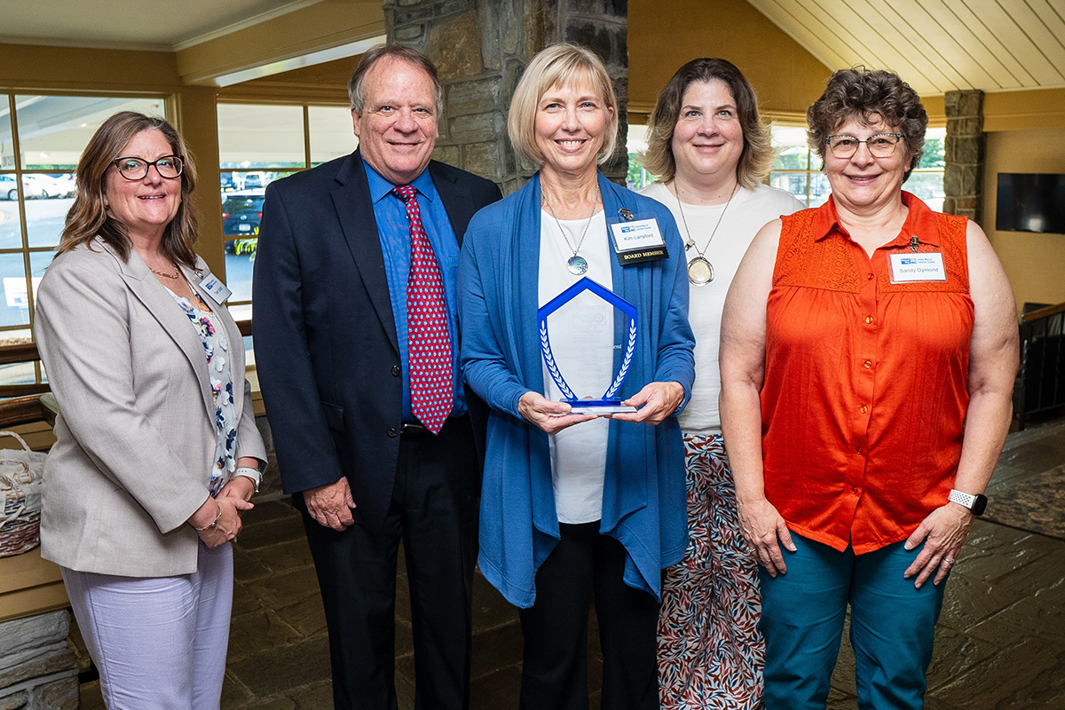 Five people pose with the United Way of Lebanon County Community Commitment Award trophy. They are standing in front of a stone fireplace.