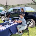 Students and faculty sit at a tent at at an exhibition, providing health care screenings and edcuation