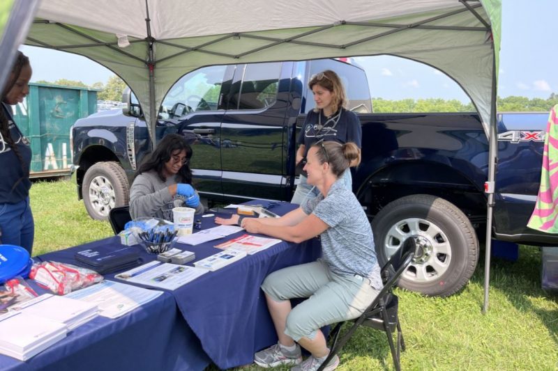 Students and faculty sit at a tent at at an exhibition, providing health care screenings and edcuation