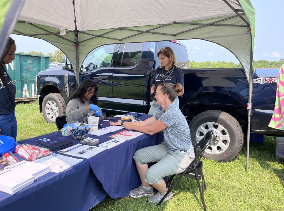 Students and faculty sit at a tent at at an exhibition, providing health care screenings and edcuation