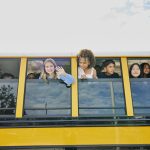 Children look out of open windows on a school bus.