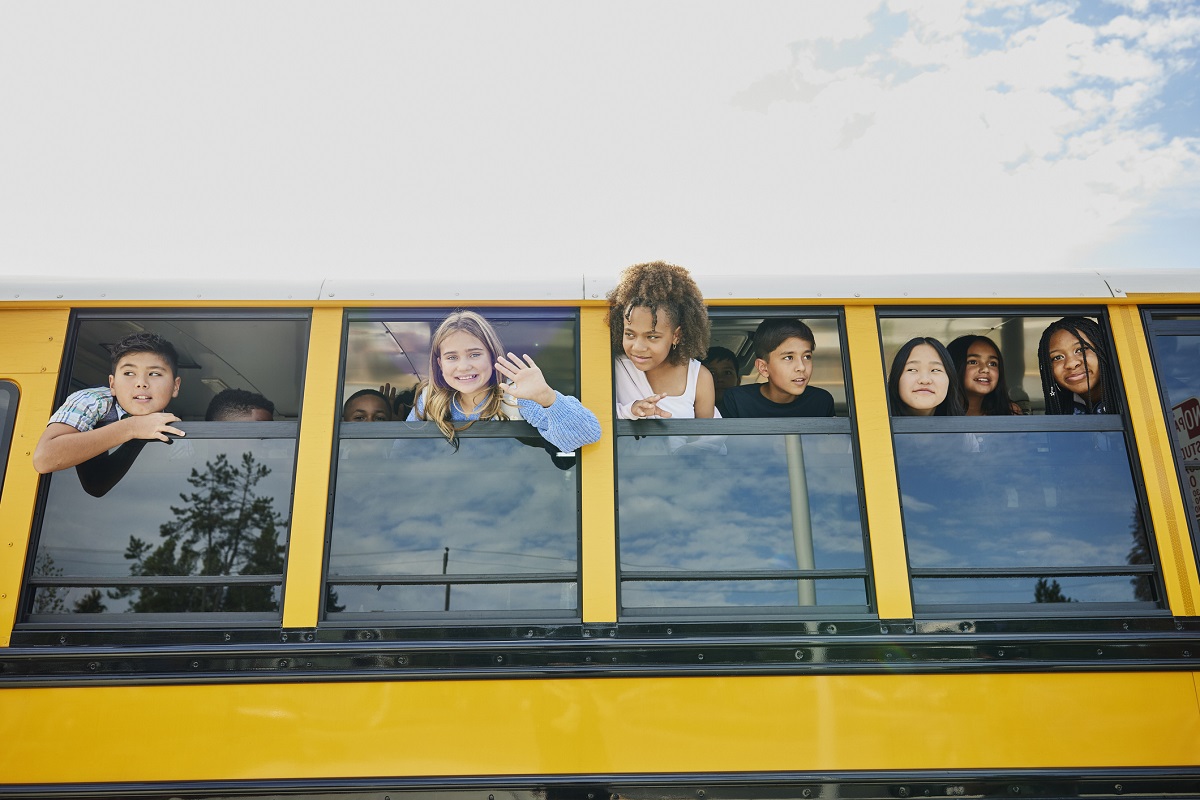 Children look out of open windows on a school bus.