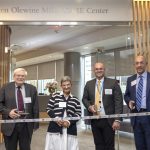 Four people pose for a photo as they prepare to ceremonially cut a ribbon.