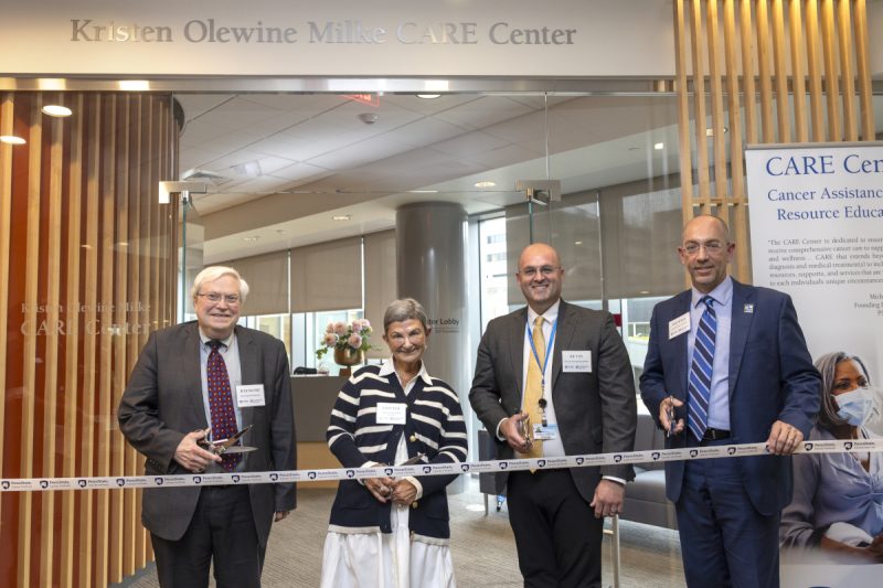 Four people pose for a photo as they prepare to ceremonially cut a ribbon.