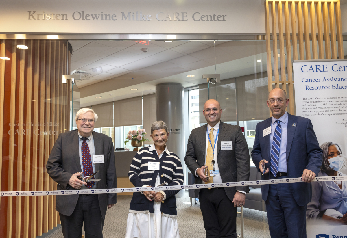 Four people pose for a photo as they prepare to ceremonially cut a ribbon.