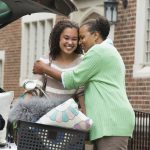 A mother and daughter hug near a car.