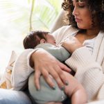 A woman sits in a chair, breastfeeding her infant child.