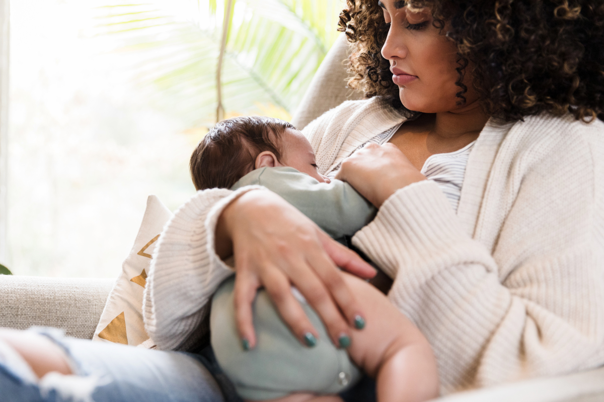 A woman sits in a chair, breastfeeding her infant child.