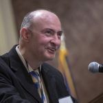 A man dressed in a suit speaks at a podium