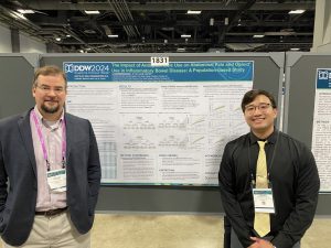 Dr. Matthew Coates and Chachrit (Poom) Khunsriraksakul, MD-PhD student, stand in front of a large printout of a research poster.