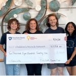 Four people smile for a photo while holding a large check from a fundraising event