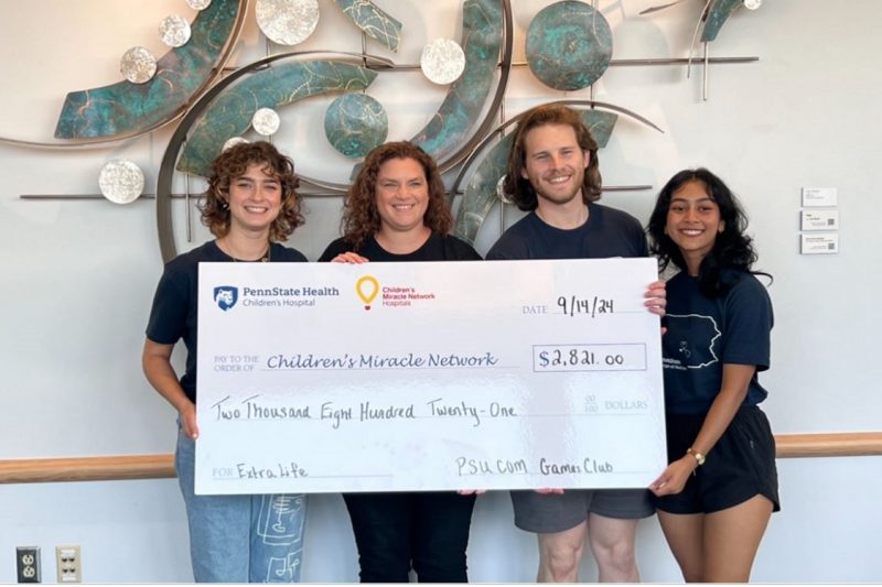 Four people smile for a photo while holding a large check from a fundraising event