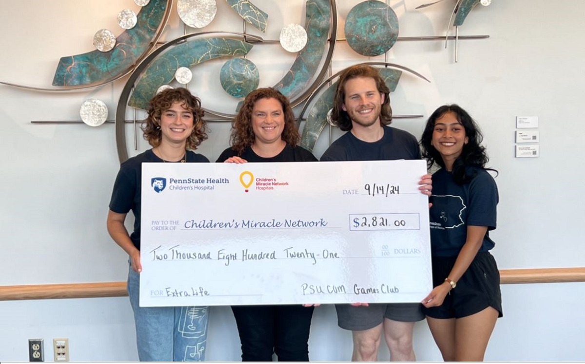 Four people smile for a photo while holding a large check from a fundraising event