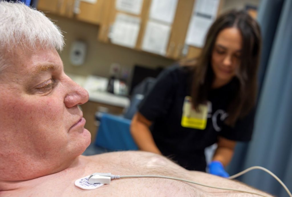 John Jones, left, looks at heart monitor leads as he gets a cardiac sonogram. Emily Kreider, is seen on the right, out of focus.