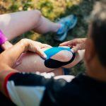 Mature man applying bandage on knee of his wife outdoor.