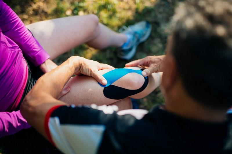 Mature man applying bandage on knee of his wife outdoor.