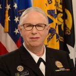 Portrait of woman wearing glasses and a military uniform. United States flag is in the background.