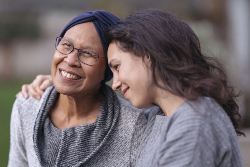 A younger woman embraces a senior woman with her right arm.