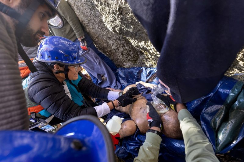 Students practice a simulated rope rescue next to climbing rocks with a mannequin