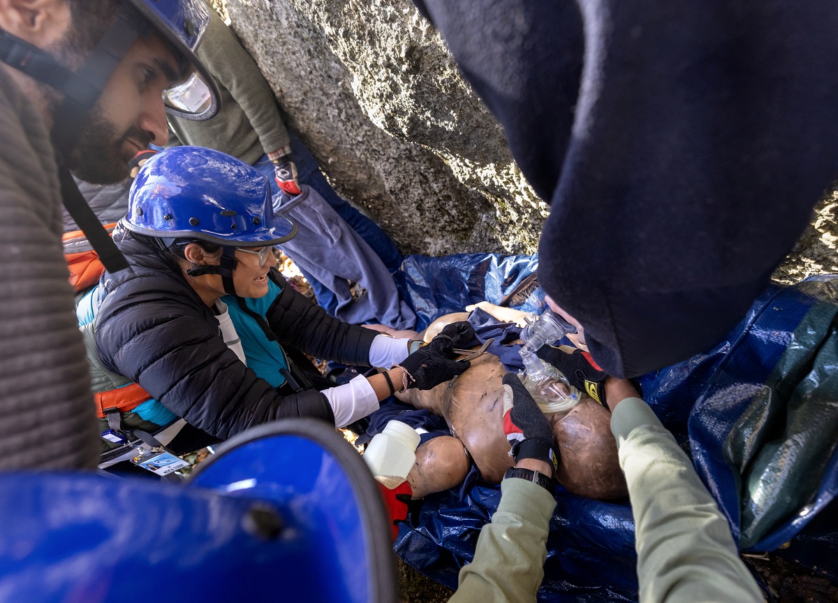 Students practice a simulated rope rescue next to climbing rocks with a mannequin