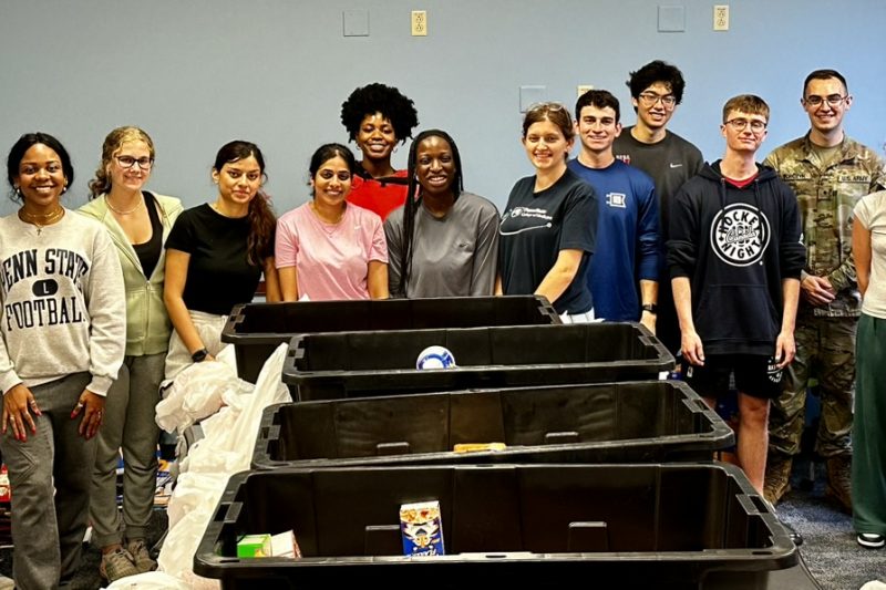 A group of Penn State students stands around food bins after packing up food parcels.