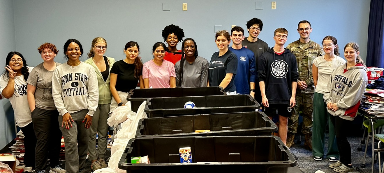 A group of Penn State students stands around food bins after packing up food parcels.