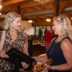 Nicole Osevala at the left holds an award while smiling and talking to a co-worker.