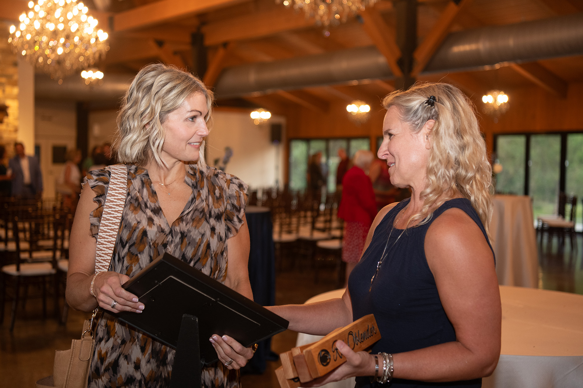 Nicole Osevala at the left holds an award while smiling and talking to a co-worker.