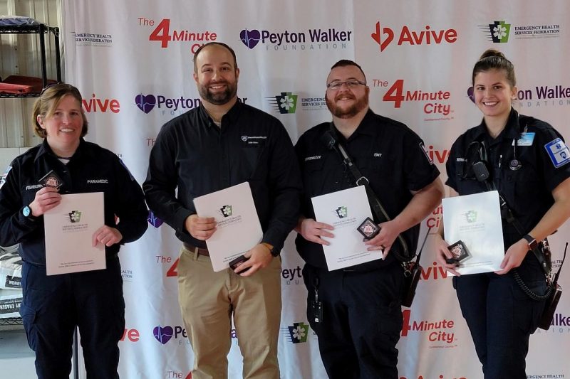 Four people pose for a photograph, each holding in front of them certificates of recognition.