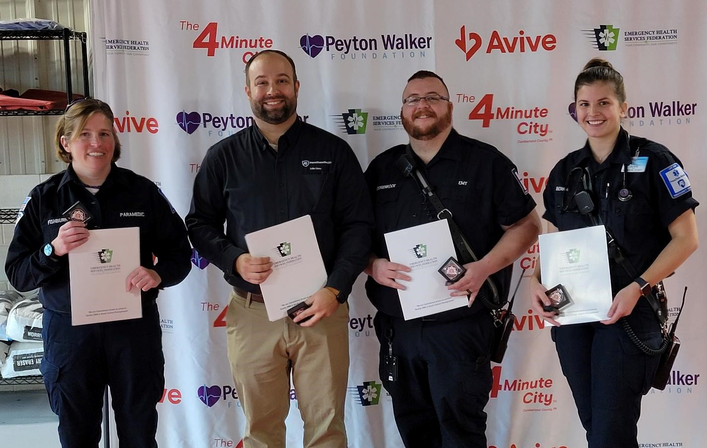 Four people pose for a photograph, each holding in front of them certificates of recognition.