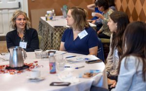 Nicole Osevala and Laura Norton sit at a table with several other participants of the Geriatric Scholars Program launch event.