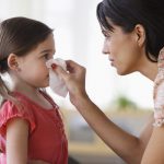 A mother wipes her daughter’s nose with a tissue.