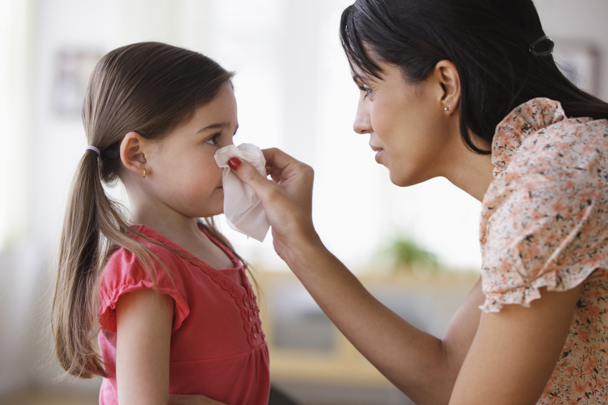 A mother wipes her daughter’s nose with a tissue.