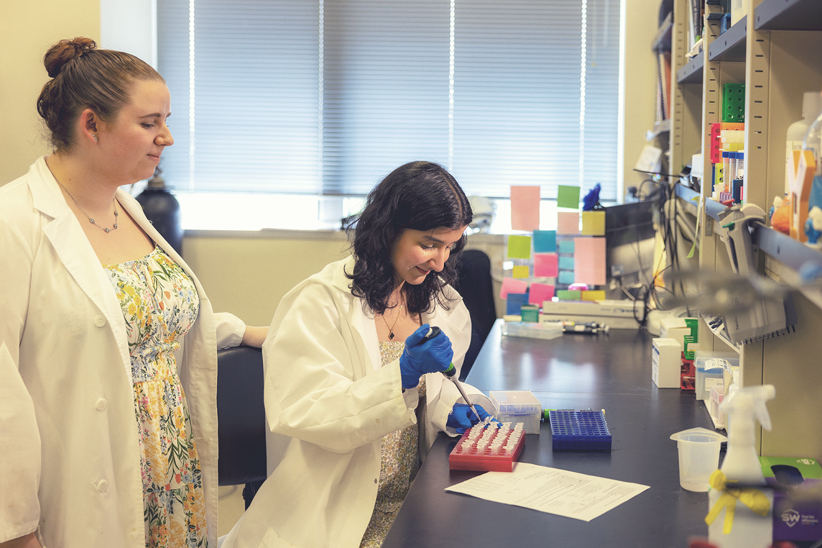 Two women wearing white coats work in a research lab