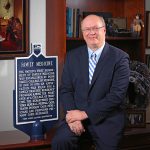 Mack Ruffin IV, MD, MPH, sits for a professional portrait next to an historical marker about the nation's first Department of Family Medicine being established at Penn State College of Medicine in 1967.